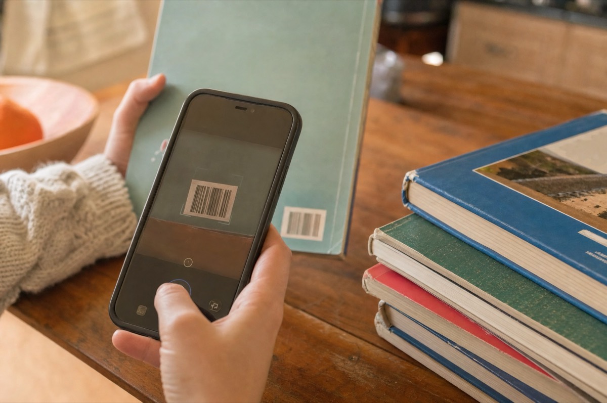 Una mano inquadra con il telefono il codice a barre sul retro di un libro di scuola, su un tavolo di cucina